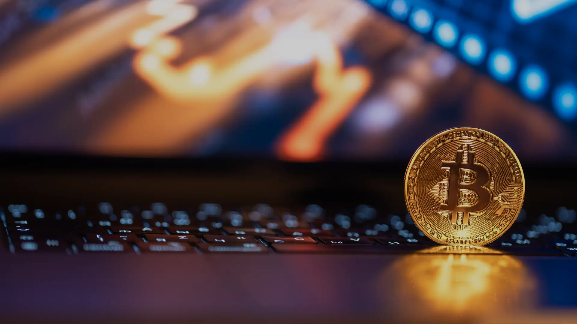 Crypto Citizenship by Investment: 2026 Guide 1 A physical gold Bitcoin coin standing on a laptop keyboard with blurred trading charts displayed on the screen.