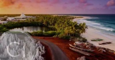 Aerial sunset view of the Nauru coastline featuring a sandy beach, traditional outrigger canoes, a small lake, and palm trees.